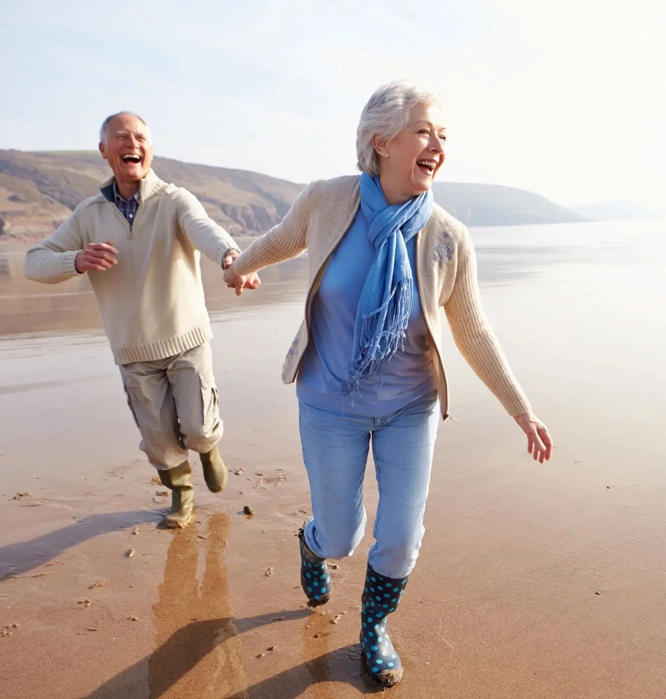 A man and woman holding hands while walking on the beach.