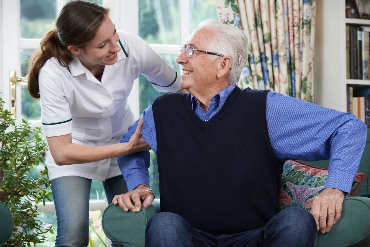 A nurse is helping an elderly man to sit in his chair.